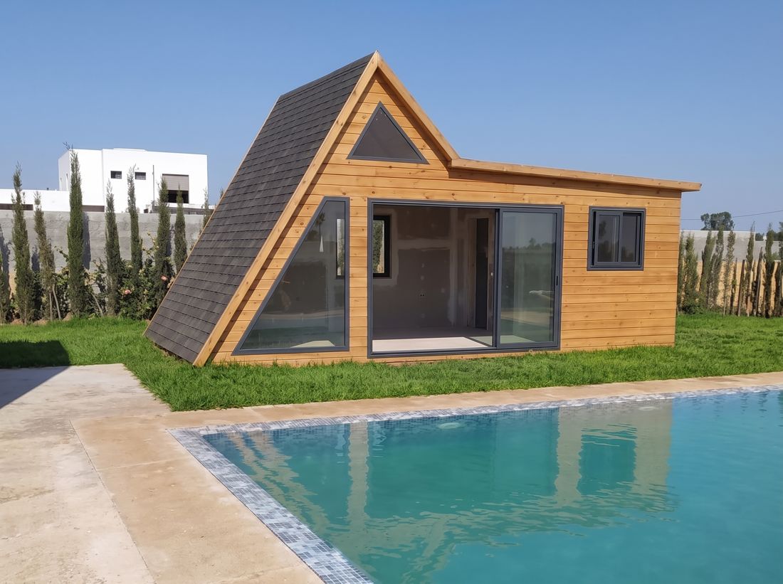 Pool house en forme de A, bardage bois et grandes baies vitrées, au bord d'une piscine